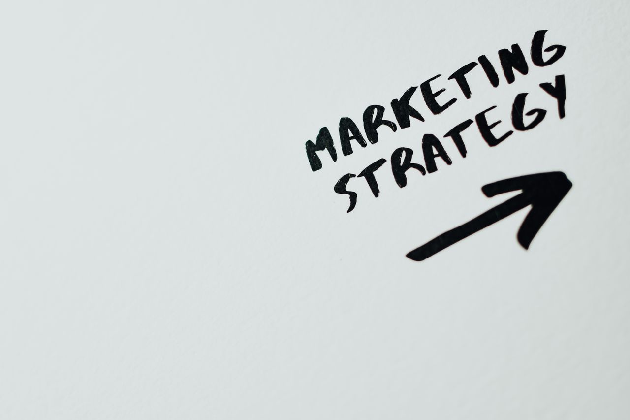 Close-up d’un texte manuscrit « Marketing Strategy » avec une flèche sur fond blanc.